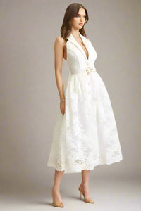 Woman wearing a white lace dress with a belt against a plain background